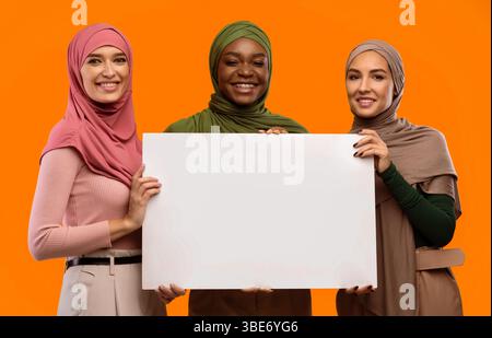 Trois musulmanes tenant une affiche vide sur fond jaune Banque D'Images