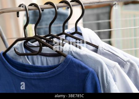 Chemises bleues et blanches douces suspendues soigneusement sur des cintres noirs dans un dégradé de couleurs doux capturant l'esthétique de la lessive et une garde-robe minimale Banque D'Images