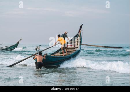 Les pêcheurs masculins vietnamiens asiatiques naviguent sur des bateaux à rames en bois en mer en Asie. Tam Thanh, province de Quang Nam, Vietnam - 10 avril 2025 Banque D'Images