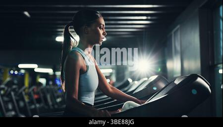 Fitness, profil et tapis roulant avec femme dans le gymnase pour l'entraînement cardio ou la routine de performance. Exercice, intense et course avec athlète indien dans l'obscurité Banque D'Images