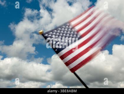Drapeau américain flou contre le ciel bleu et les nuages blancs, drapeau américain vagues dans le vent, mouvement flou contre un ciel clair, évoquant le mouvement, l'énergie et le symbolisme national Banque D'Images