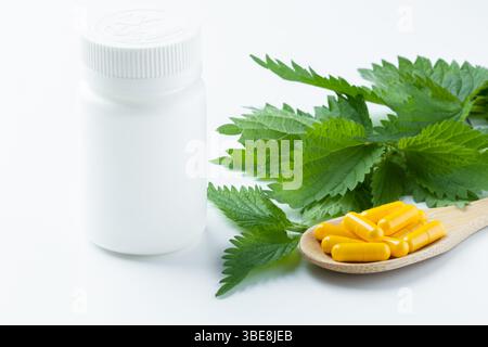 Les feuilles d'ortie sont disposées autour d'une bouteille de supplément jaune simple sur une surface minimaliste blanche. Banque D'Images