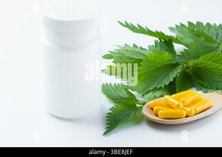 Les feuilles d'ortie sont disposées autour d'une bouteille de supplément jaune simple sur une surface minimaliste blanche. Banque D'Images