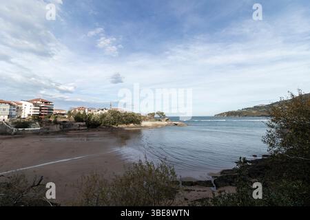 Scène côtière tranquille avec une plage calme, l'océan, les bâtiments et un ciel nuageux Banque D'Images