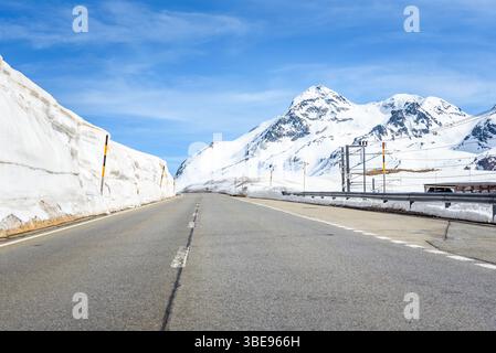 Tronçon vide d'une route de col de montagne à travers un paysage enneigé sous le ciel bleu au début du printemps Banque D'Images