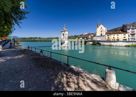 Vue panoramique sur un pont suspendu enjambant le Rhône à Seyssel, en France, avec une église pittoresque et des bâtiments dynamiques au bord de la rivière Banque D'Images