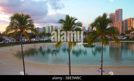 Lagon tropical avec palmiers et horizon de la ville, vue panoramique sur la plage à Honolulu au coucher du soleil. Banque D'Images
