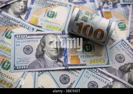 Gros plan sur les billets de 100 dollars roulés et dispersés. Une image en gros plan de billets de 100 dollars américains, avec un paquet soigneusement enroulé placé parmi les billets dispersés. Banque D'Images
