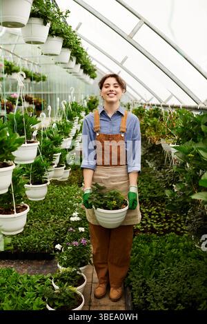 La jeune femme a tendance à fleurir les plantes tout en profitant de son temps dans la serre. Banque D'Images