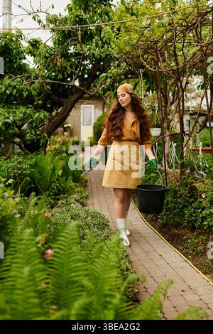 Une jeune femme dans un tablier et un foulard a tendance à luxuriante plantes tout en portant un seau. Banque D'Images