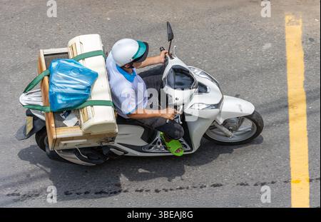 Un homme porte un climatiseur complet sur une moto le long d'une rue de la ville, Vietnam Banque D'Images