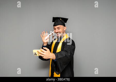 Heureux diplômé faisant appel vidéo montrant le diplôme tout en portant la robe et la casquette Banque D'Images