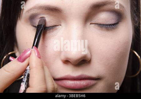 Maquilleur traite le maquillage sur le visage du modèle. Elle peint les ombres du modèle des paupières supérieures Banque D'Images