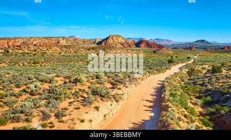 Vol aérien à travers les formations Red Rock Sagebrush Plain et Winding Dirt Road Banque D'Images