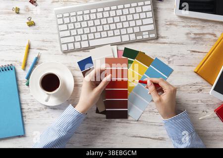 Concepteur Web choisissant des couleurs à partir de nuances au bureau en bois. Lieu de travail de bureau avec clavier d'ordinateur et tasse de café. Conception de l'interface utilisateur de mobi Banque D'Images