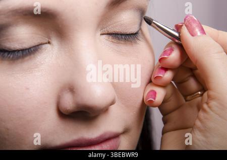 Maquilleur traite le maquillage sur le visage du modèle. Elle peint les ombres du modèle des paupières supérieures Banque D'Images