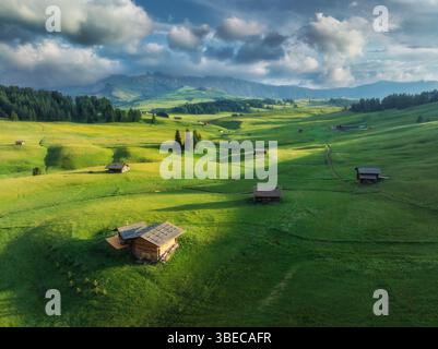 Vue aérienne de la plus grande prairie alpine de haute altitude d'europe, l'alpe di siusi, cabanes en bois nichées dans un paysage verdoyant au coucher du soleil. Vue de dessus de Banque D'Images