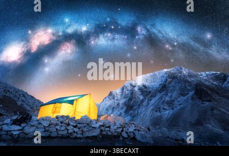 Voie lactée acrh sur tente jaune incandescente dans les montagnes enneigées à la nuit étoilée. Randonnée et trekking au Népal. Paysage coloré avec tente, STA lumineux Banque D'Images