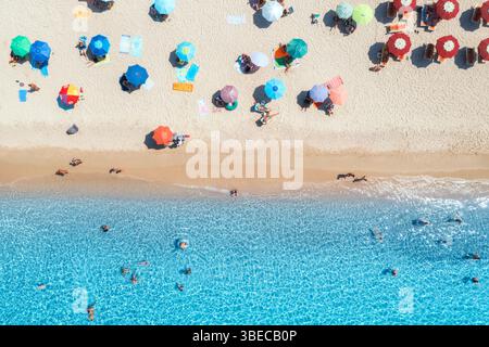 Vue aérienne de parasols colorés sur la plage de sable, nager les gens dans la mer bleue le jour ensoleillé d'été. Sardaigne, Italie. Paysage tropical avec azur clair Banque D'Images