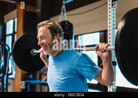 Un homme soulève une barre de poids lourd avec un sourire sur son visage il porte une chemise bleue et il s'amuse Banque D'Images