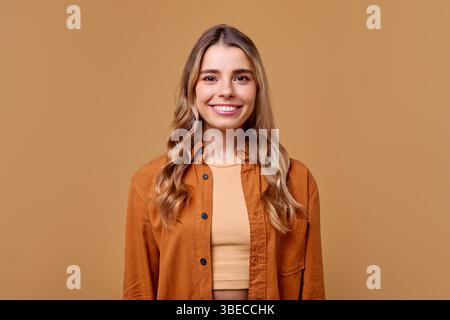 Une jeune femme joyeuse et vibrante avec de longs cheveux ondulés fluides, vêtue d'une tenue tendance et élégante, pose en toute confiance avec un sm chaleureux et accueillant Banque D'Images