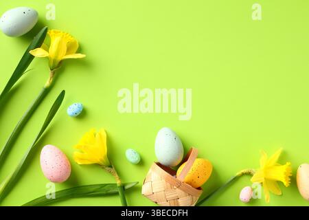 Joyeuses Pâques composition de pose à plat. Oeufs de Pâques colorés et fleurs de jonquille jaunes sur fond vert. Banque D'Images