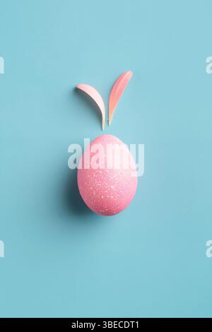 Œuf de pâques rose avec oreilles de lapin en pétales de fleurs sur fond turquoise. Concept de carte de Pâques créative. Banque D'Images