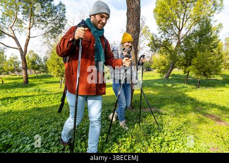 Jeune couple jouissant d'un mode de vie sain, pratiquant la marche nordique ensemble dans un parc verdoyant animé rempli d'arbres et d'herbe Banque D'Images