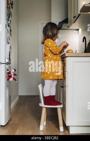 Fille caucasienne épluchant des mandarines sur le comptoir de cuisine. Alimentation saine de l'enfant. Stimulation immunitaire avec de la vitamine c. Banque D'Images