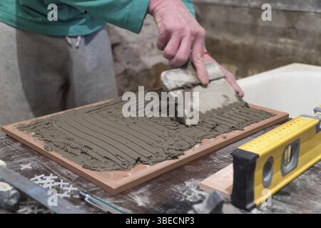 L'ouvrier applique de l'adhésif de ciment sur les carreaux. Travaux de finition, mise au point floue. La technologie de pose de carreaux Banque D'Images