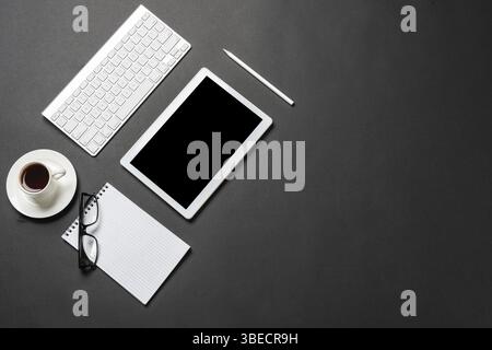 Vue de dessus du lieu de travail moderne avec tablette. Surface noire plate avec clavier, tasse de café et ordinateur portable. Vue de dessus de l'espace de travail de coworking et Banque D'Images