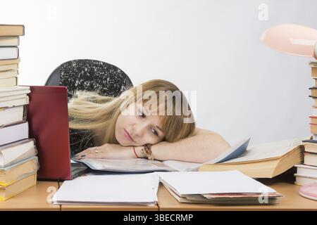 L'élève fille posé sa tête sur sa main remplies de livres et de documents se trouvant sur le bureau Banque D'Images