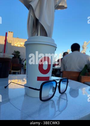 Tasse à café et lunettes de soleil sur une table de café en plein air avec un fond flou de personnes profitant du soleil à Istanbul. Banque D'Images