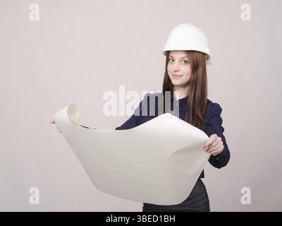 Jeune femme architecte au casque debout avec les bleus dans la main Banque D'Images