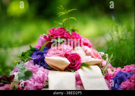 Gros plan d'un arrangement floral dans un cimetière de fleurs rose pastel et violettes avec deux rubans de deuil de couleur crème avec des gouttelettes d'eau après un R. Banque D'Images