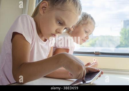 Deux filles soeurs assis dans le train à l'phone Banque D'Images