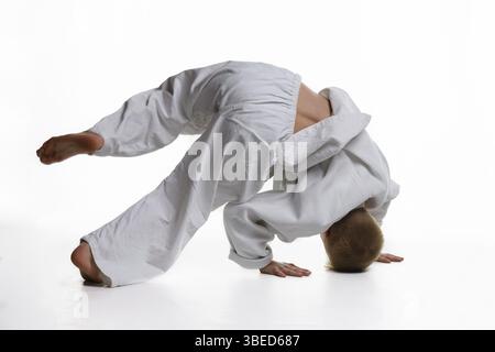 Judo garçon qui fait de l'échauffement se tournoyant autour de lui tout en se tenant sur sa tête Banque D'Images