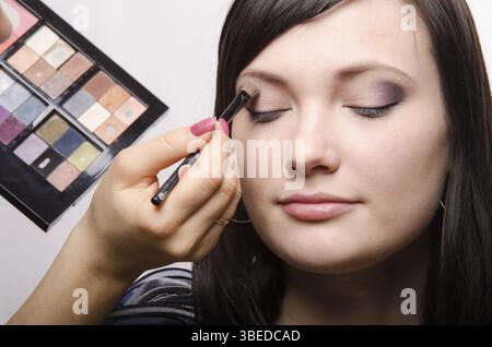 Maquilleur traite le maquillage sur le visage du modèle. Elle peint les ombres du modèle des paupières supérieures Banque D'Images