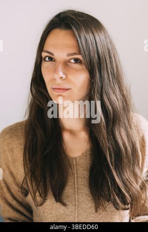 Jeune jeune femme jolie du millénaire à la maison assise sur le canapé. Portrait sûr et sain. Longs cheveux bruns et grands yeux belle femme. Banque D'Images