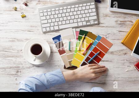 Concepteur Web choisissant des couleurs à partir de nuances au bureau en bois. Lieu de travail de bureau avec clavier d'ordinateur et tasse de café. Conception de l'interface utilisateur de mobi Banque D'Images