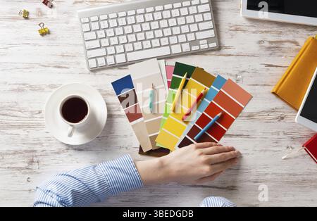 Concepteur Web choisissant des couleurs à partir de nuances au bureau en bois. Lieu de travail de bureau avec clavier d'ordinateur et tasse de café. Conception de l'interface utilisateur de mobi Banque D'Images