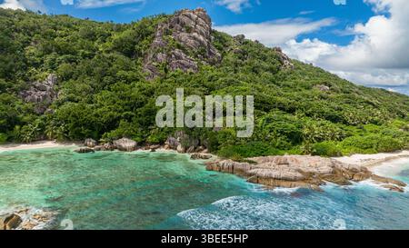 Littoral avec végétation tropicale et eaux turquoises claires le long d'une plage de sable. La Digue, Seychelles. Banque D'Images