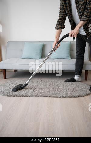 homme aspirant la moquette dans le salon, nettoyage du sol. Propriétaire faisant des travaux ménagers utilisant un appareil électroménager. Banque D'Images