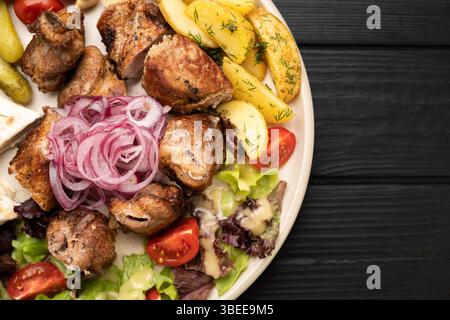 Succulentes brochettes de viande grillée accompagnées de légumes frais, de pommes de terre frites croustillantes et d'oignons marinés acidulés, capturés en gros plan. Banque D'Images