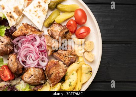 morceaux de porc grillé juteux avec oignon rouge, pommes de terre frites, champignons, tomates cerises et cornichons, servis avec du pain pita. vue de dessus. Gros plan Banque D'Images