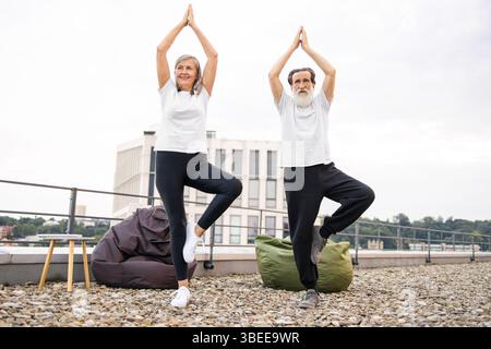 Couple senior pratiquant le yoga pose sur le toit dans un cadre extérieur calme Banque D'Images