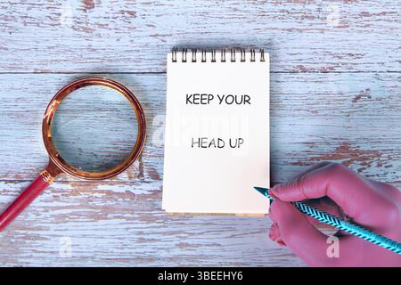 Mots conceptuels GARDEZ LA TÊTE HAUTE sur une note manuscrite placée à côté d'une loupe sur de vieux tableaux. Banque D'Images