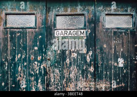 Vieille porte de garage patinée avec peinture verte pelable et signe Garagem. Entrée de garage portugaise vintage, surface en bois vieilli, architecture rustique, Banque D'Images