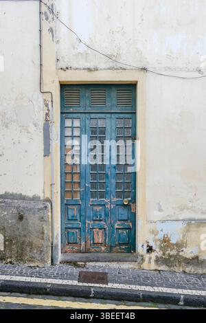 Porte en bois bleu vintage avec panneaux de verre sur le bâtiment blanc. Architecture portugaise, peinture altérée, entrée traditionnelle, rue pavée, arche Banque D'Images