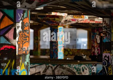 Des graffitis vifs recouvrent les piliers d'un undercroft à Londres. La scène artistique urbaine met en valeur la créativité et la couleur dans un espace public. Banque D'Images